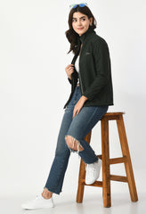 Waylene's stylish outdoor wear featured with the model sitting on a wooden stool, olive green jacket unzipped showing black shirt underneath.
