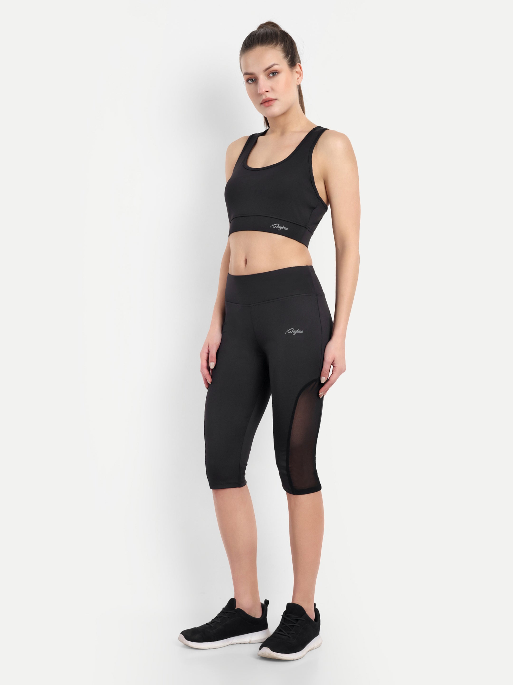 Waylene's black Capri and sports bra tracksuit set for women, perfect for yoga and gym. Model stands confidently with hands on hips, showcasing the mesh panel design on Capri and fitted sports bra.