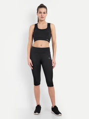 Model in Waylene's black yoga Capri and sports bra set, standing straight with hands by her sides, ideal for gym workouts. The outfit emphasizes a minimalist design with a subtle logo on the hip.