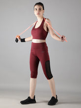 Model using resistance bands while wearing Waylene's wine track suit with stylish Capri tights, showcasing the flexibility and fit during a workout.