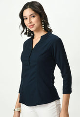Waylene's dark navy blue top on a model, highlighting the V-neck and 3/4 sleeves with buttoned cuffs, paired with elegant white pants for a chic professional look.