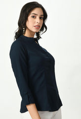 Woman modeling Waylene's dark navy blue blouse with a classic collar and buttoned front, showcasing the slim fit and structured design of the top, complemented by white trousers.