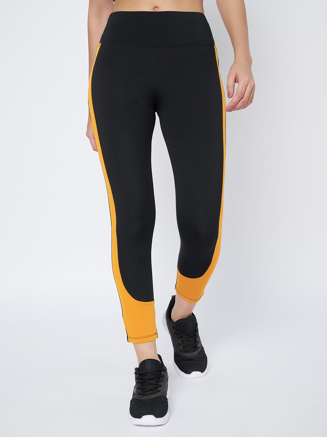 Front view of Waylene's high-performance black and mustard gym tights for women showing the streamlined design and vibrant side stripes, paired with black sneakers.