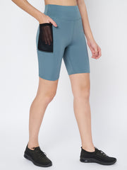 Model inserting a smartphone into the side pocket of Waylene's teal sports shorts, emphasizing practicality and ease during exercise.