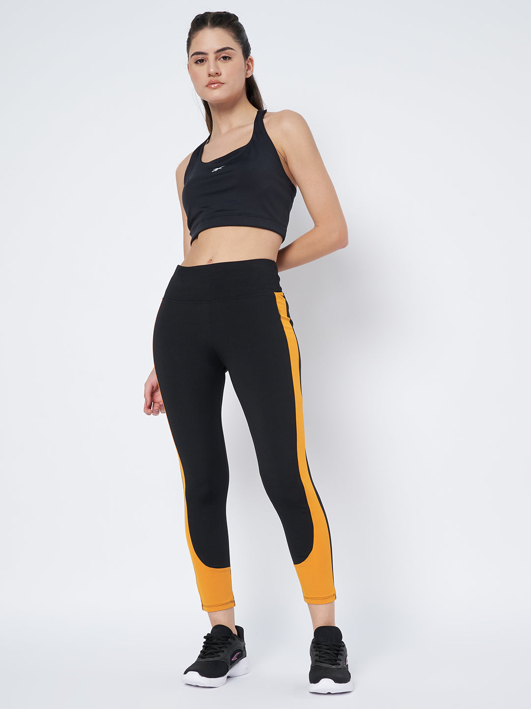 Full-body angled view of a model in Waylene's high-performance black and mustard gym tights for women, showing off the high waist and sleek silhouette against a minimalist background.