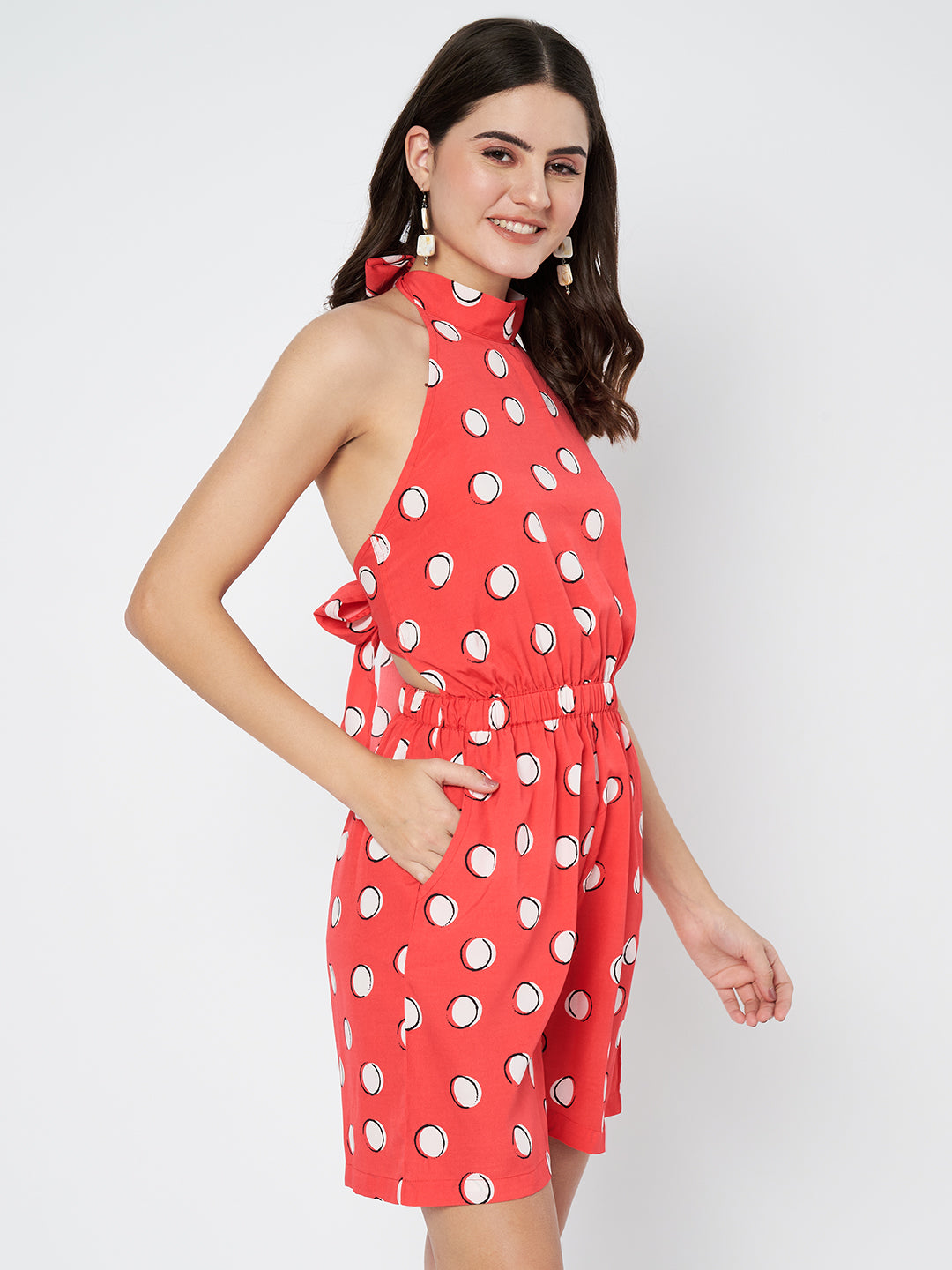 Waylene's red polka dot jumpsuit with a halter neck and a cinched waist, model smiling and hands on hips, front view.
