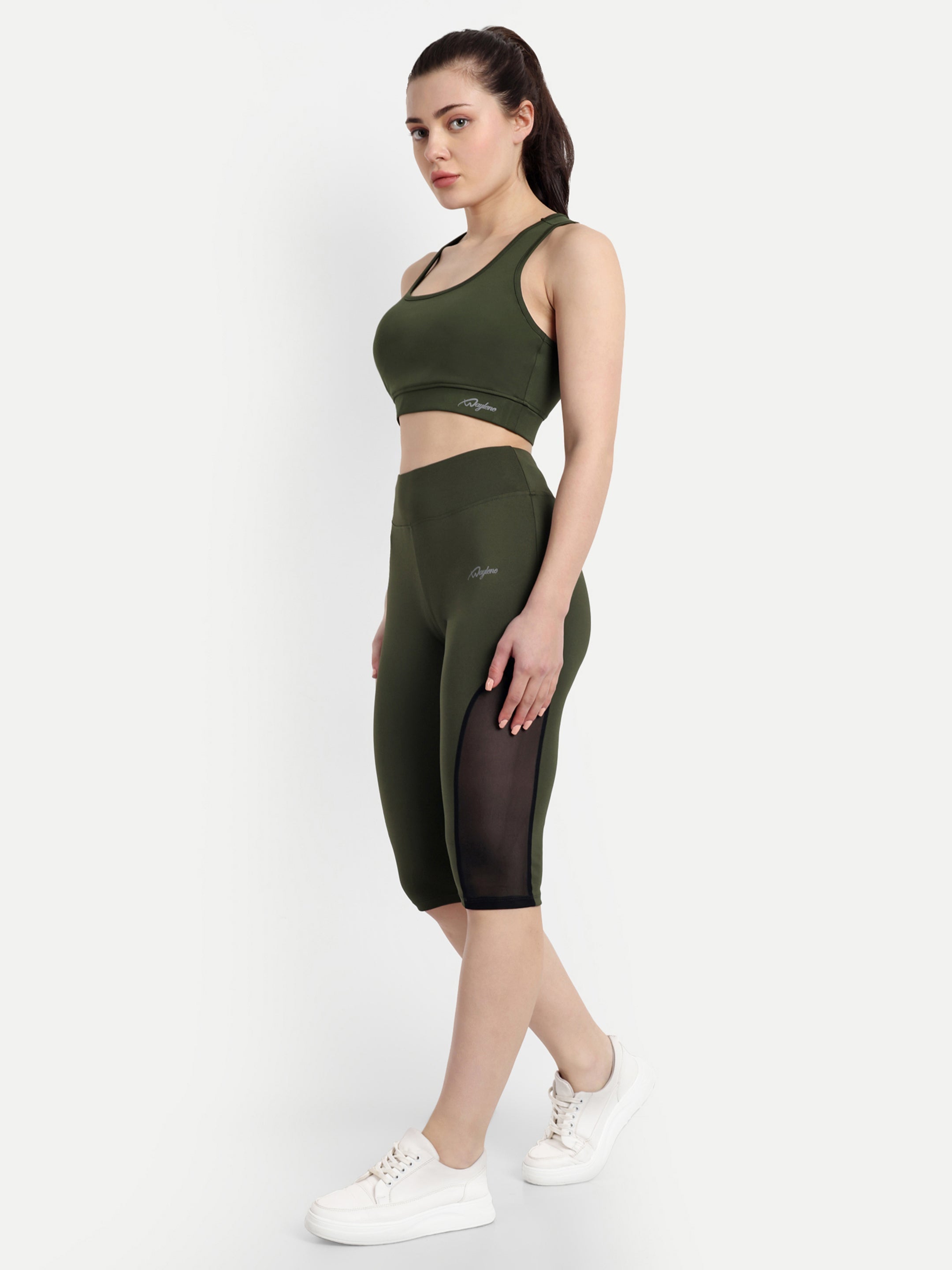 Model posing in Waylene's olive green sports bra and capri tights, side view showcasing the mesh detail and contour of the fabric.