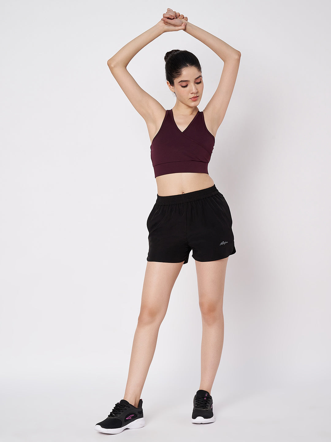 Female model in Waylene's black polyester shorts stretching with arms raised, paired with a maroon crop top, demonstrating the comfort and flexibility of the activewear.